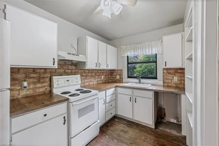 Kitchen featuring sink, white appliances, white cabinetry, and backsplash