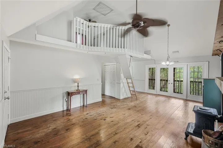 Living room with ceiling fan with notable chandelier, high vaulted ceiling, a wood stove, and hardwood / wood-style flooring