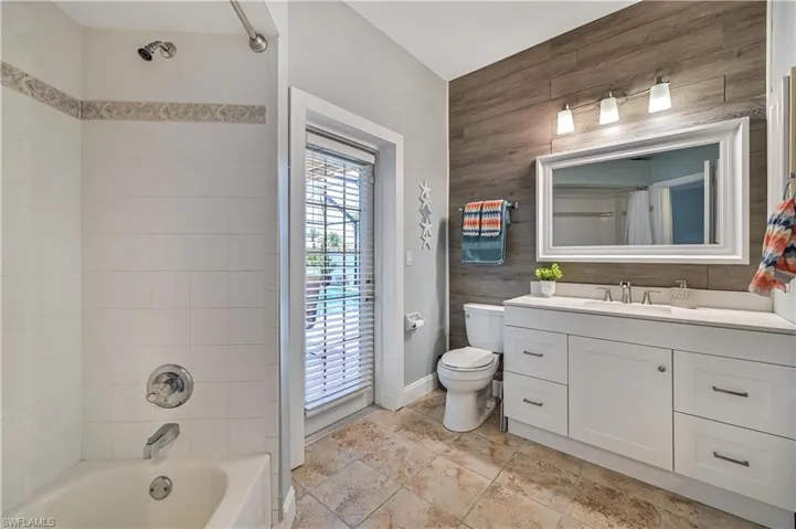 Bathroom with shower / tub combo with curtain, toilet, wooden walls, baseboards, and vanity
