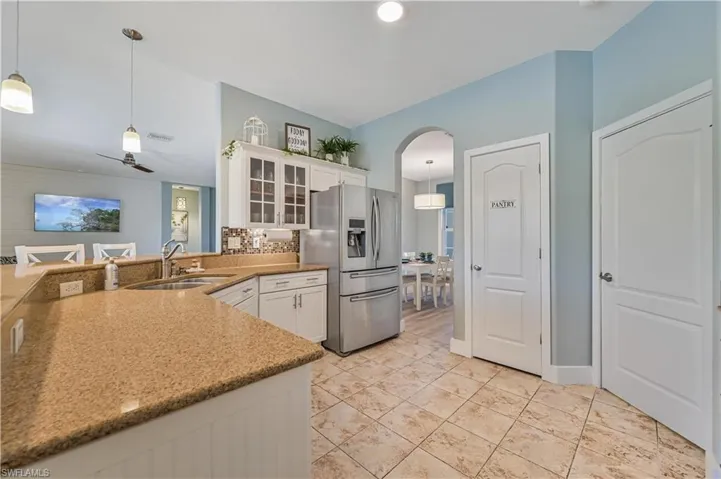 Kitchen featuring pendant lighting, stainless steel refrigerator with ice dispenser, a sink, arched walkways, and glass insert cabinets