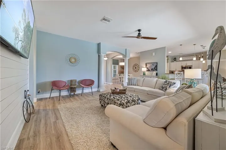 Living room with light wood finished floors, baseboards, ornate columns, arched walkways, and a ceiling fan