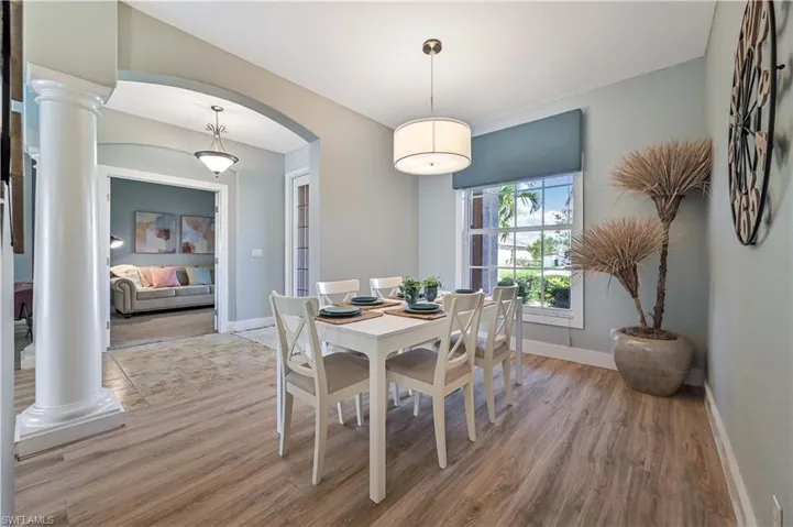 Dining space with arched walkways, light wood finished floors, baseboards, and ornate columns