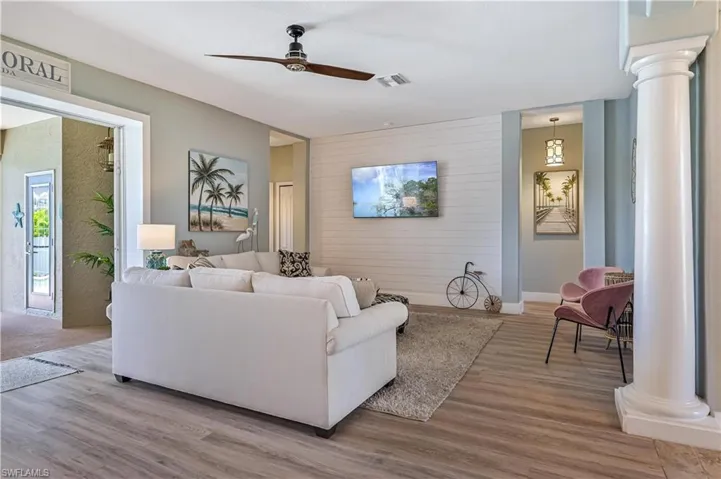 Living area with a ceiling fan, decorative columns, wood finished floors, and visible vents
