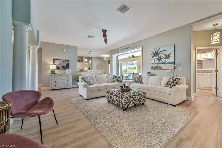Living area with visible vents, baseboards, light wood-style floors, and ornate columns
