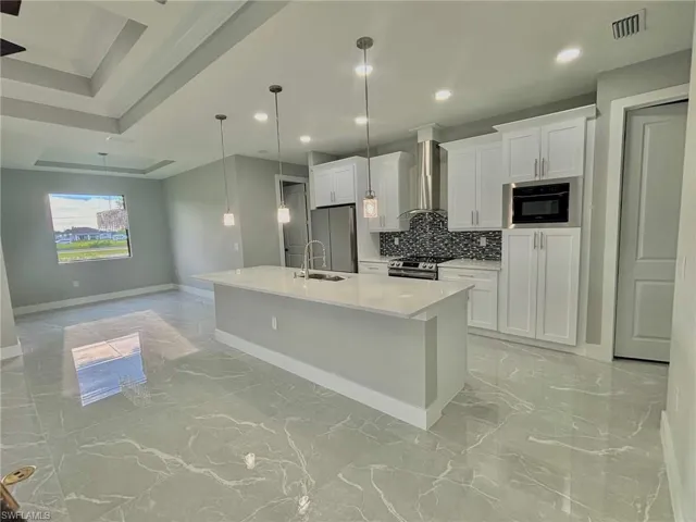 Kitchen with wall chimney range hood, decorative backsplash, appliances with stainless steel finishes, a center island with sink, and light tile patterned flooring