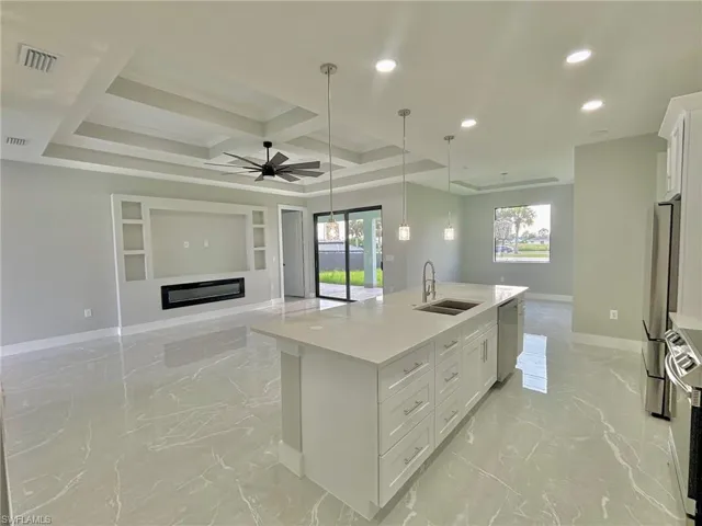 Kitchen with coffered ceiling, sink, an island with sink, white cabinets, and ceiling fan
