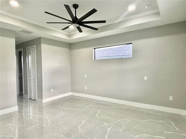 Tiled empty room featuring ceiling fan, a raised ceiling, and ornamental molding