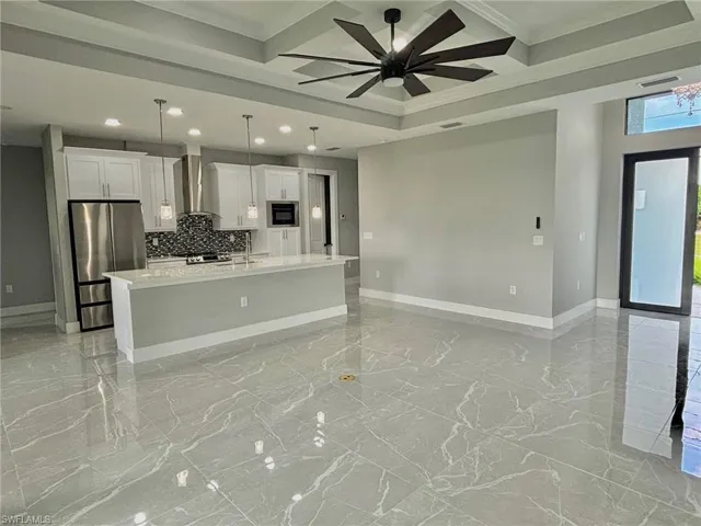 Kitchen featuring crown molding, stainless steel fridge, hanging light fixtures, a center island with sink, and wall chimney range hood