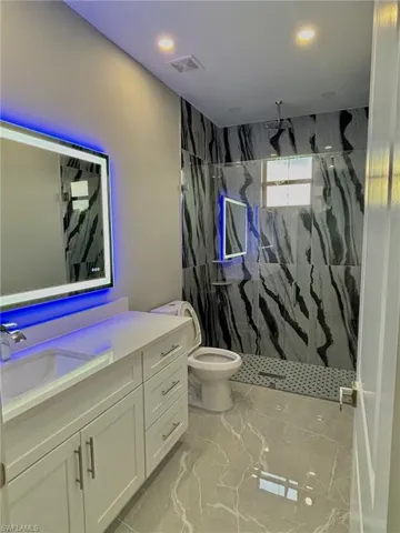 Bathroom with toilet, a tile shower, vanity, and tile patterned floors