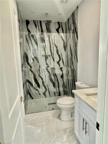 Bathroom featuring tile patterned floors, a tile shower, vanity, and toilet