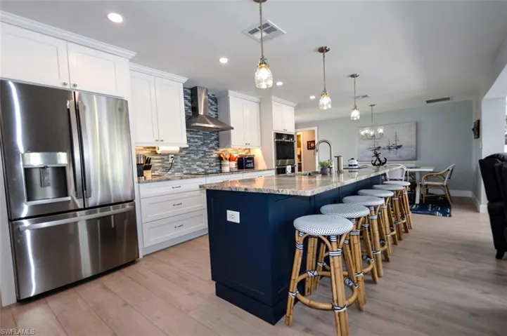 Kitchen featuring white cabinetry, a kitchen island with sink, wall chimney exhaust hood, and stainless steel appliances