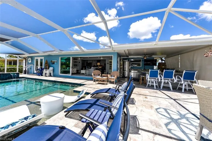 View of pool featuring ceiling fan, a patio area, an outdoor bar, and glass enclosure