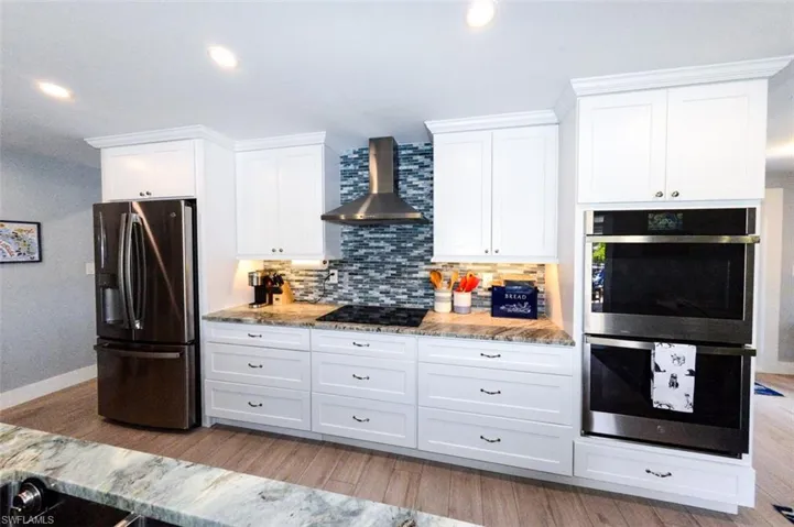 Kitchen with white cabinetry, wall chimney exhaust hood, backsplash, and appliances with stainless steel finishes