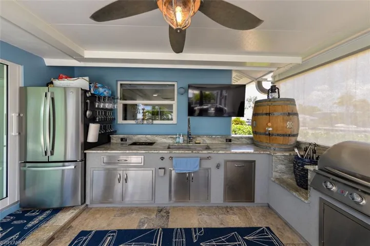 Kitchen featuring stainless steel fridge, sink, ceiling fan, and light stone counters