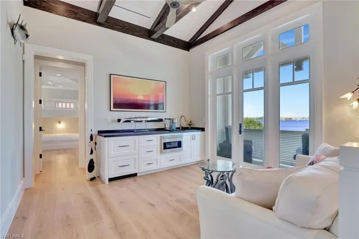 Living room with wooden ceiling, light wood-type flooring, vaulted ceiling with beams, sink, and a water view