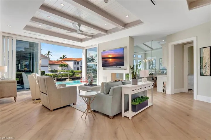 Living room with vaulted ceiling, wood ceiling, ceiling fan with notable chandelier, and light wood flooring