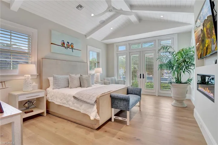 Primary Bedroom with light hardwood flooring, multiple windows, fireplace, french doors to outdoor deck, wood ceiling detail, and ceiling fan