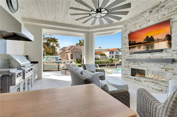 View of patio / terrace with an outdoor stone fireplace, a grill, an outdoor kitchen, and ceiling fan, and remote screens