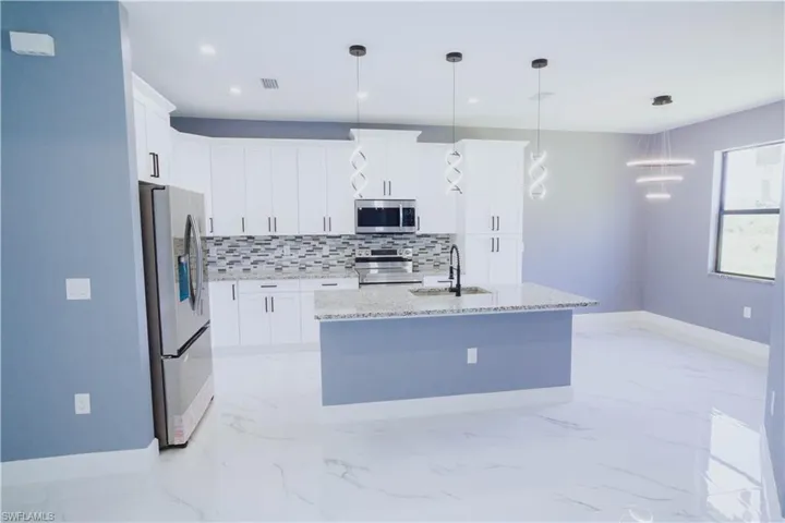 Kitchen with light marble finish floors, tasteful backsplash, stainless steel appliances, hanging light fixtures, and white cabinetry
