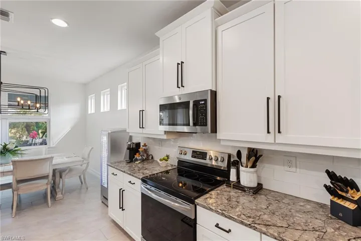 Kitchen with light stone counters, stainless steel appliances, decorative backsplash, and white cabinets