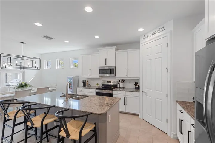 Kitchen featuring sink, white cabinetry, stainless steel appliances, light stone countertops, and a kitchen island with sink