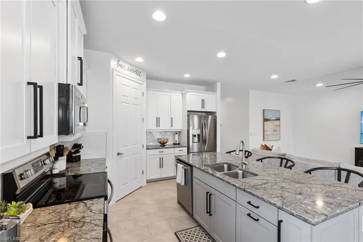 Kitchen with sink, white cabinetry, stainless steel appliances, light stone countertops, and a center island with sink