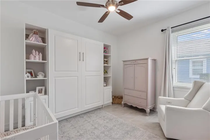 Tiled bedroom featuring a nursery area and ceiling fan