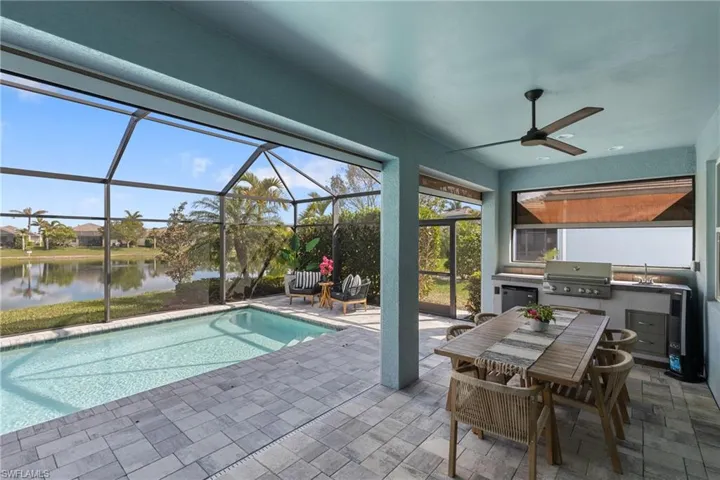 View of swimming pool featuring a water view, a lanai, exterior kitchen, and a patio area