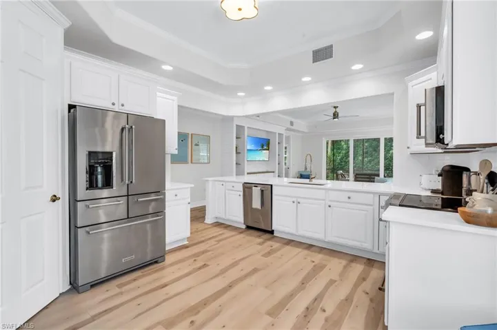 Kitchen featuring a raised ceiling, stainless steel appliances, crown molding, white cabinets, and light wood finished floors