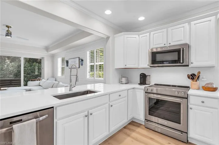 Kitchen featuring stainless steel appliances, open floor plan, white cabinets, light wood-style floors, and light stone counters