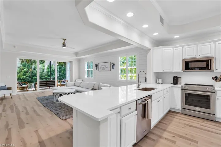 Kitchen featuring a tray ceiling, open floor plan, stainless steel appliances, white cabinets, and recessed lighting