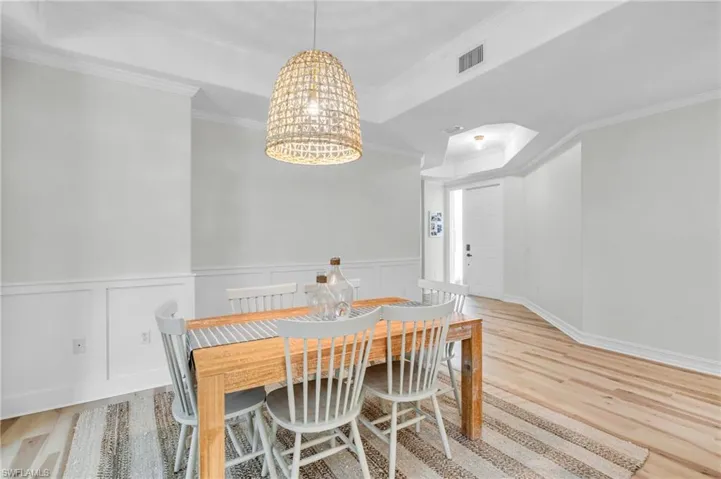 Dining area featuring ornamental molding, wainscoting, a decorative wall, a tray ceiling, and hanging lights