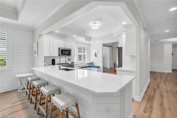 Kitchen featuring a peninsula, light wood-type flooring, crown molding, white cabinetry, and a raised ceiling