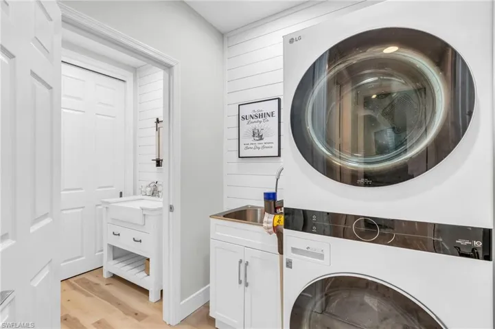 Laundry area with stacked washer / dryer, light wood-style flooring, wood walls, and cabinet space