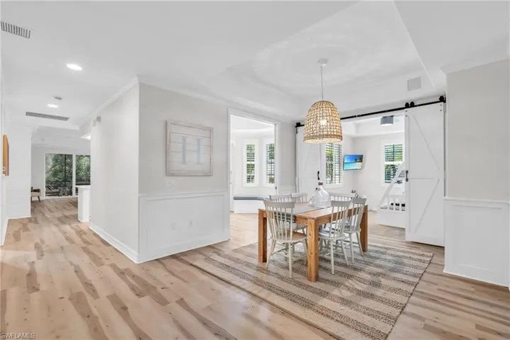 Dining area featuring light wood-type flooring, a barn door, a wainscoted wall, ornamental molding, and recessed lighting