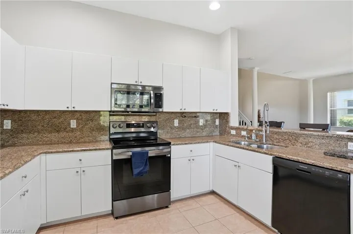 Kitchen featuring stainless steel appliances, white cabinets, light stone counters, light tile patterned floors, and tasteful backsplash