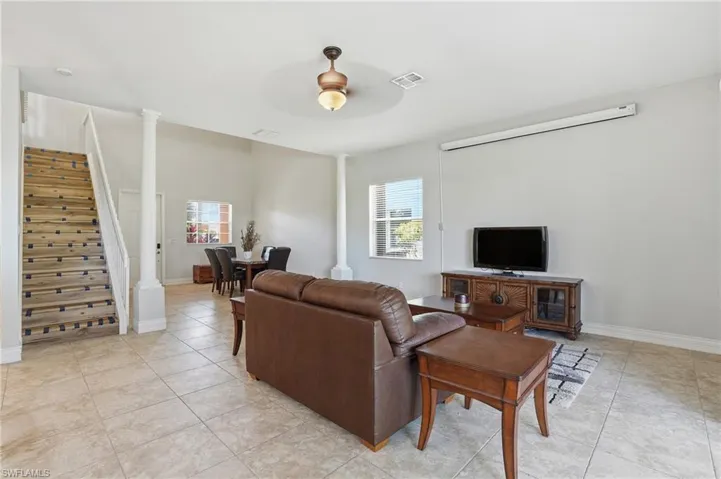 Living area featuring stairway, ceiling fan, decorative columns, and light tile patterned floors