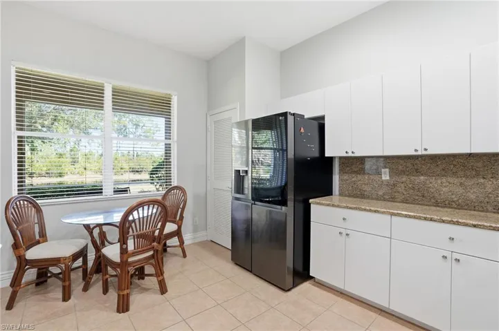 Kitchen with stainless steel refrigerator with ice dispenser, white cabinetry, light stone countertops, and tasteful backsplash
