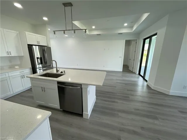 Kitchen with open floor plan, white cabinets, appliances with stainless steel finishes, a center island with sink, and dark wood finished floors