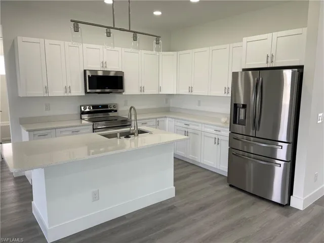 Kitchen with appliances with stainless steel finishes, white cabinetry, dark wood finished floors, light stone counters, and recessed lighting