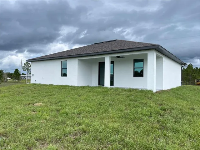 Back of property featuring stucco siding, ceiling fan, a patio, roof with shingles, and a yard