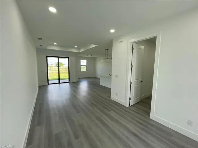 Empty room with a tray ceiling, dark wood-style flooring, and recessed lighting