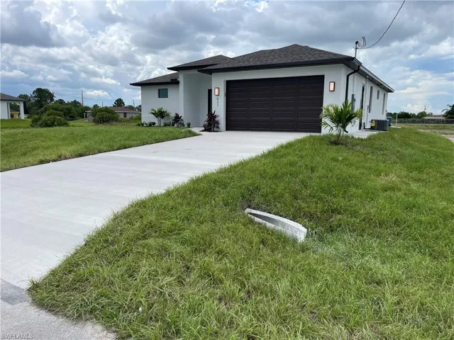 View of front of house with concrete driveway, a garage, stucco siding, and a front lawn