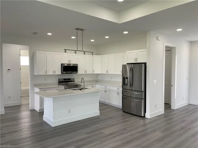Kitchen with appliances with stainless steel finishes, white cabinets, decorative light fixtures, recessed lighting, and a kitchen island with sink