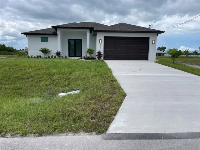 View of front facade featuring stucco siding, roof with shingles, driveway, an attached garage, and a front yard