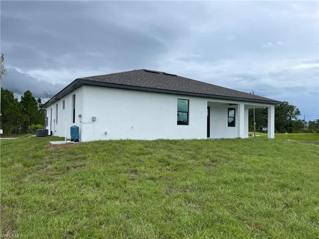 Rear view of property with a lawn, stucco siding, a shingled roof, and a patio area