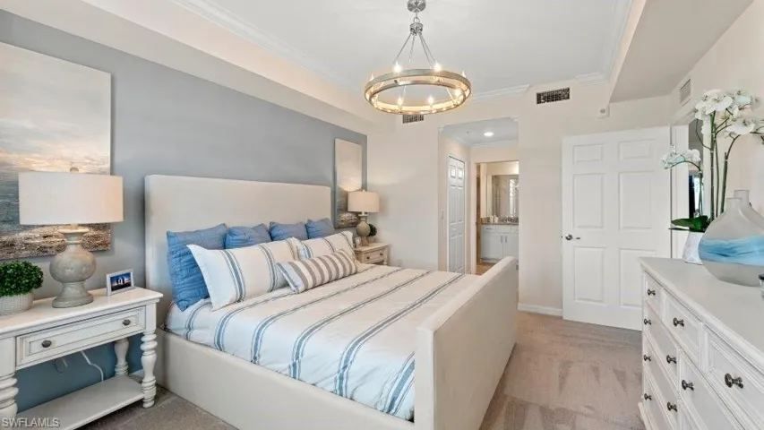 Bedroom featuring a chandelier, light colored carpet, crown molding, and ensuite bath