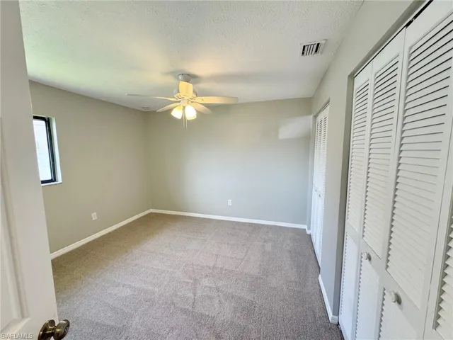 Guest bedroom 2 with a textured ceiling, carpet floors, ceiling fan, and multiple closets