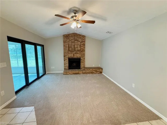 Unfurnished living room featuring ceiling fan, vaulted ceiling, light carpet, and a brick fireplace
