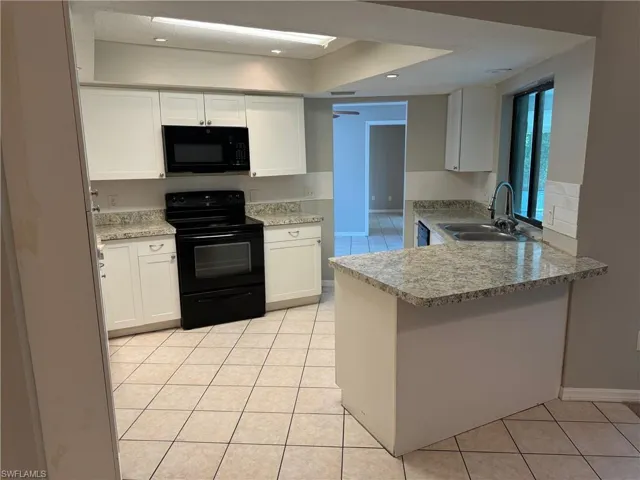 Kitchen with white cabinetry, sink, kitchen peninsula, light tile patterned flooring, and black appliances